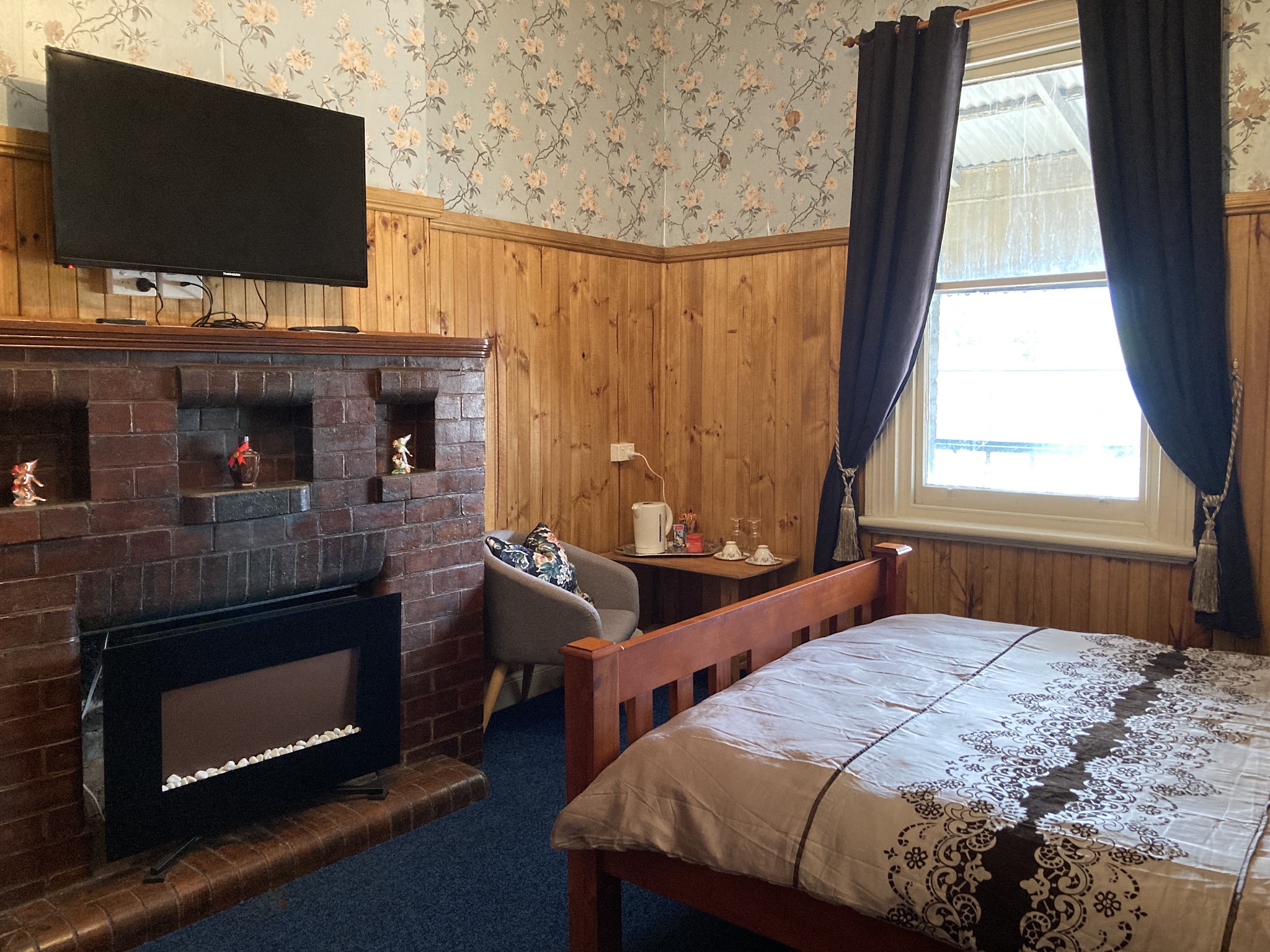 A guest room at Hunters Hotel with a made bed, brick fireplace, timber panelling, floral wallpaper and a tea tray
